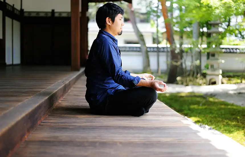 Zazen meditation on a temple veranda overlooking a tranquil Japanese garden.
