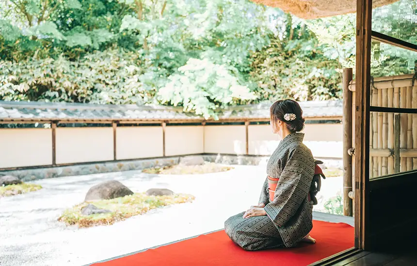 A rear view of people with serene expressions, looking at a kare-sansui (dry landscape) garden. This photo should convey a meditative atmosphere in a quiet space, symbolizing inner peace and concentration.
