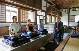 Zazen meditation session in a traditional Japanese temple with participants and a guiding monk.