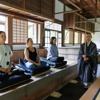 Zazen meditation session in a traditional Japanese temple with participants and a guiding monk.