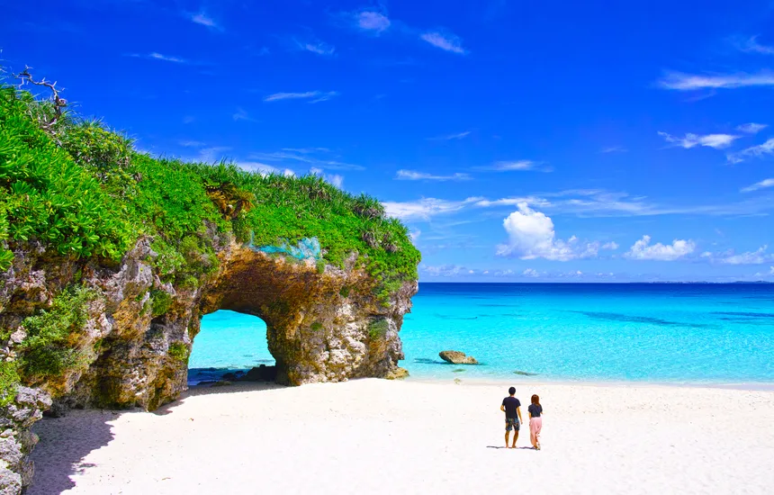 People happily beach walking against the backdrop of Okinawa's clear blue sea and white sandy beach.